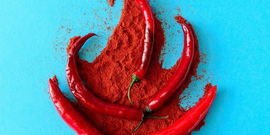 Kokonaisia punaisia chilipalkoja ja hienoa punaista chilijauhetta levitettynä kirkkaan turkoosille taustalle